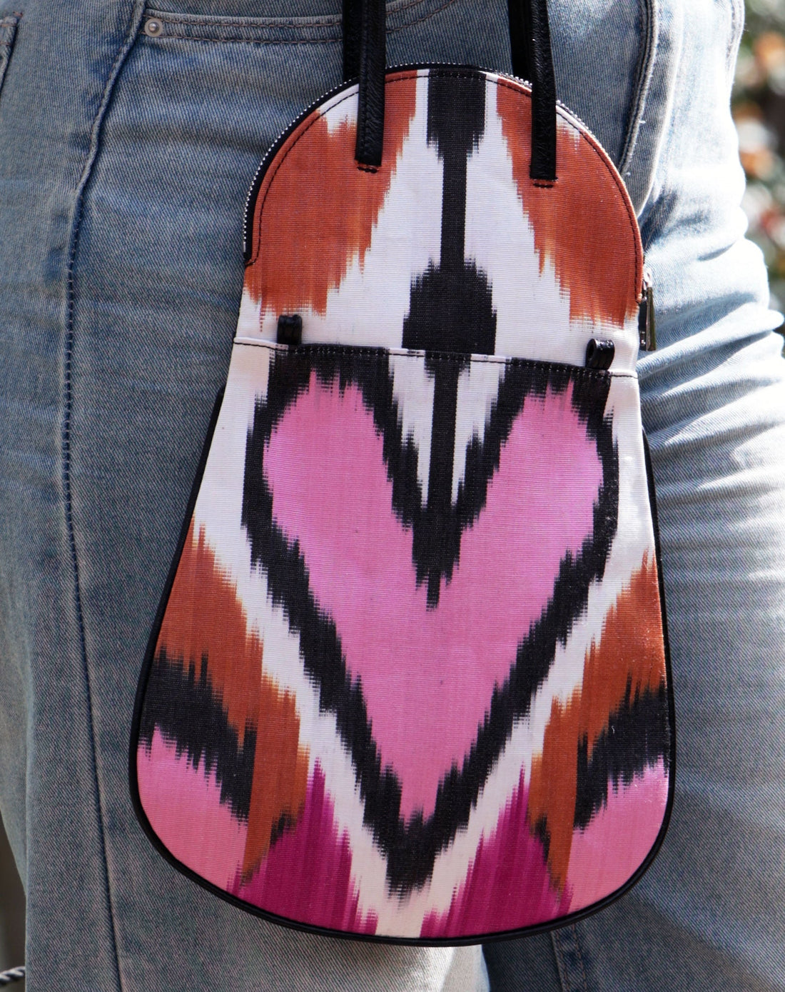 small fold-over flap handbag with pink, fuchsia, rust ornage and black ikat silk desgin on a white background with black leather straps and reverse side.