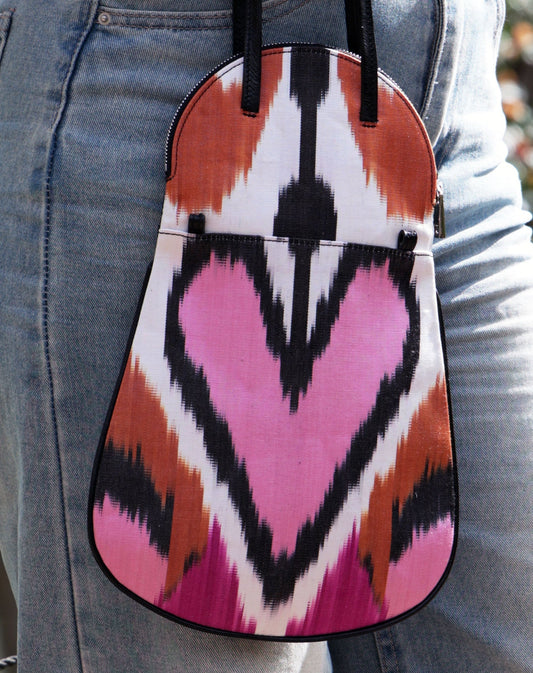 small fold-over flap handbag with pink, fuchsia, rust ornage and black ikat silk desgin on a white background with black leather straps and reverse side.